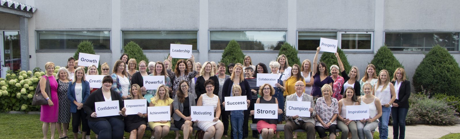 A large group of business women stand together, holding signs with words of encouragement and motivation