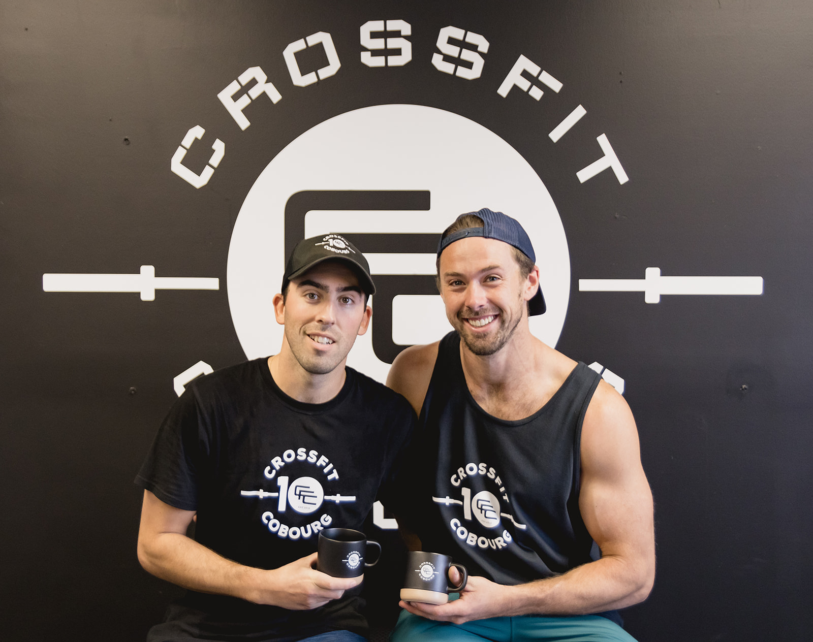 Two business owners pose in front of their gym logo